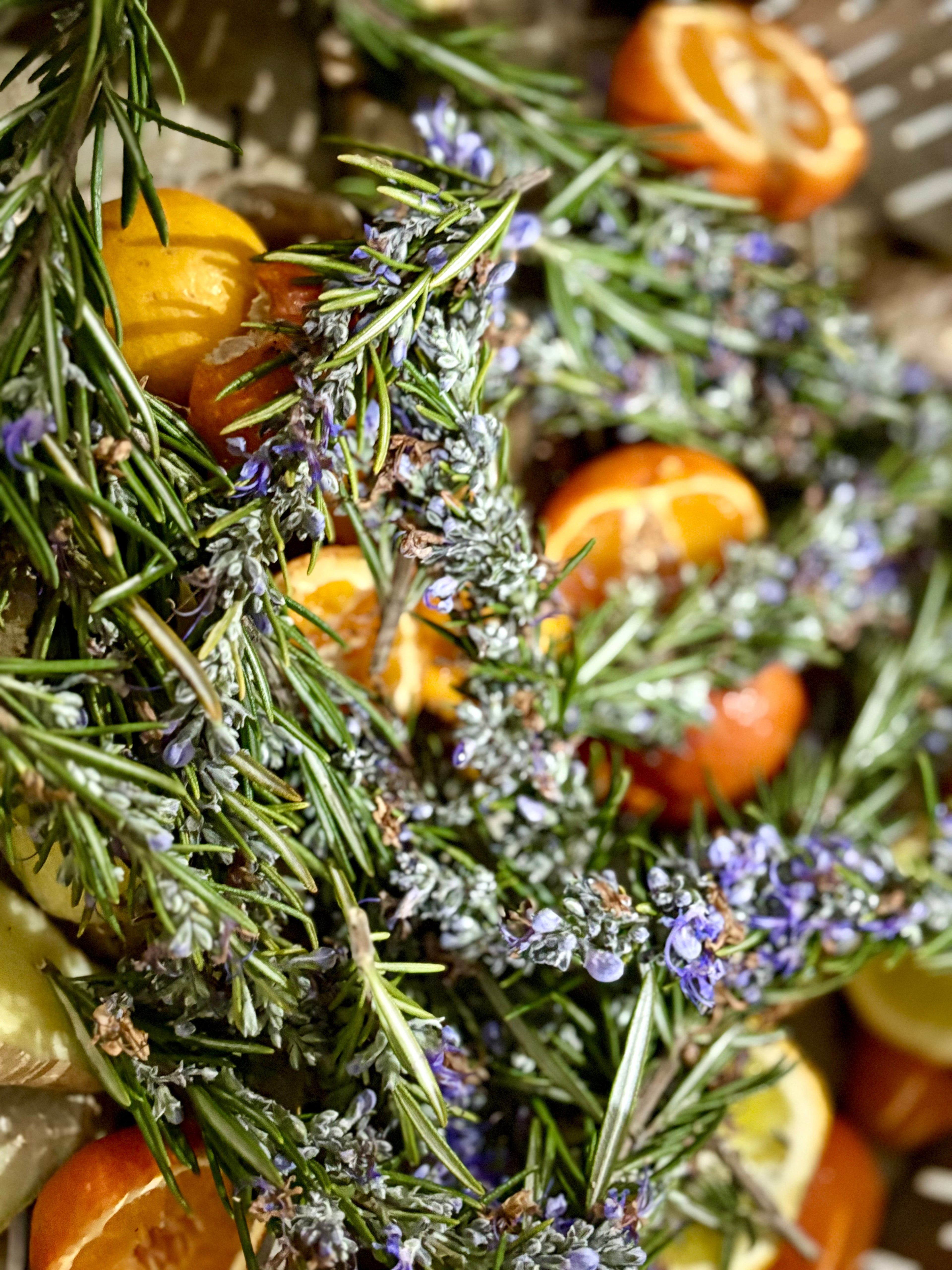 Decorative arrangement of lavender, rosemary, and tangerines on a stone surface.